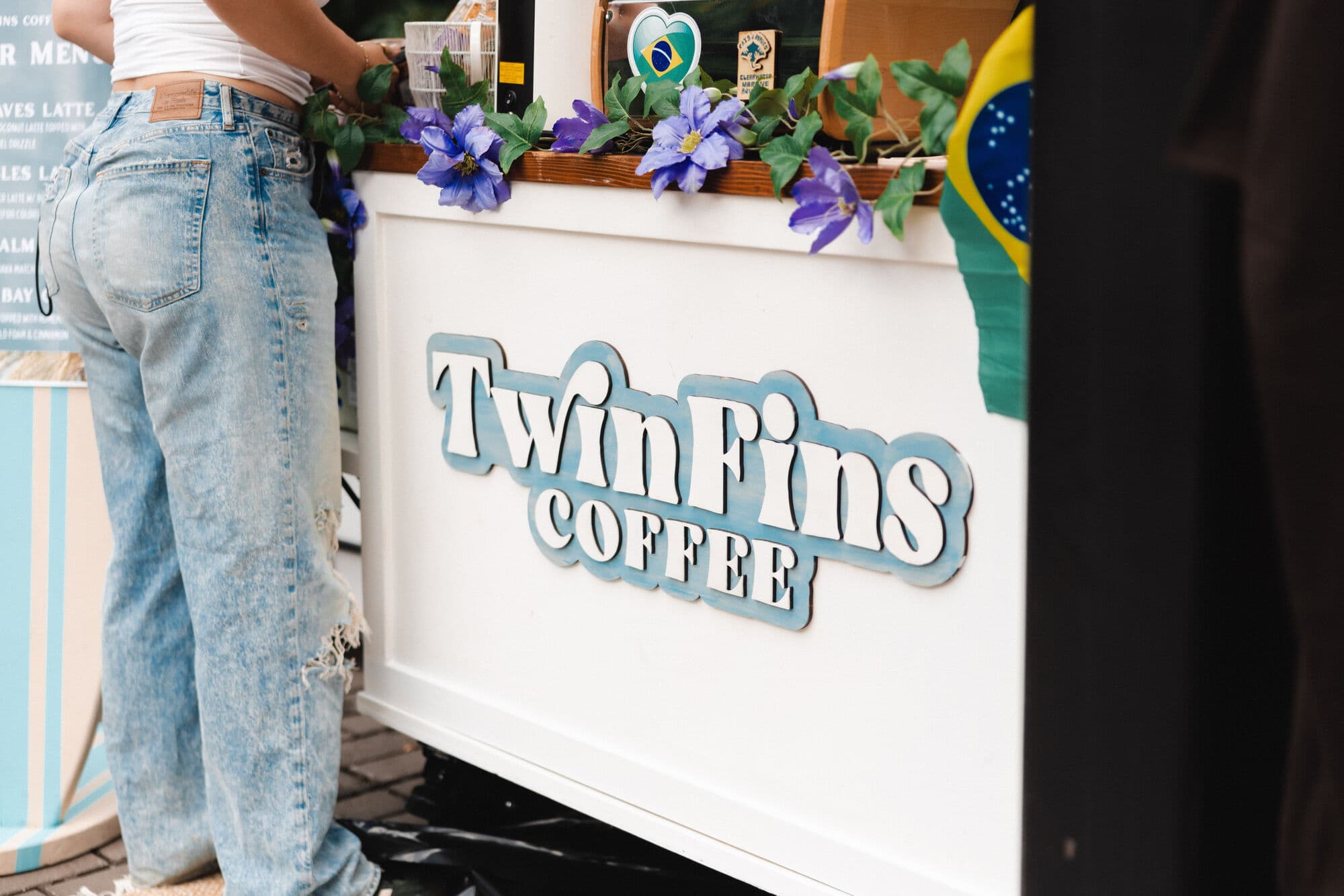 The Twin Fins Coffee cart, its teal logo panel trimmed with fresh flowers
