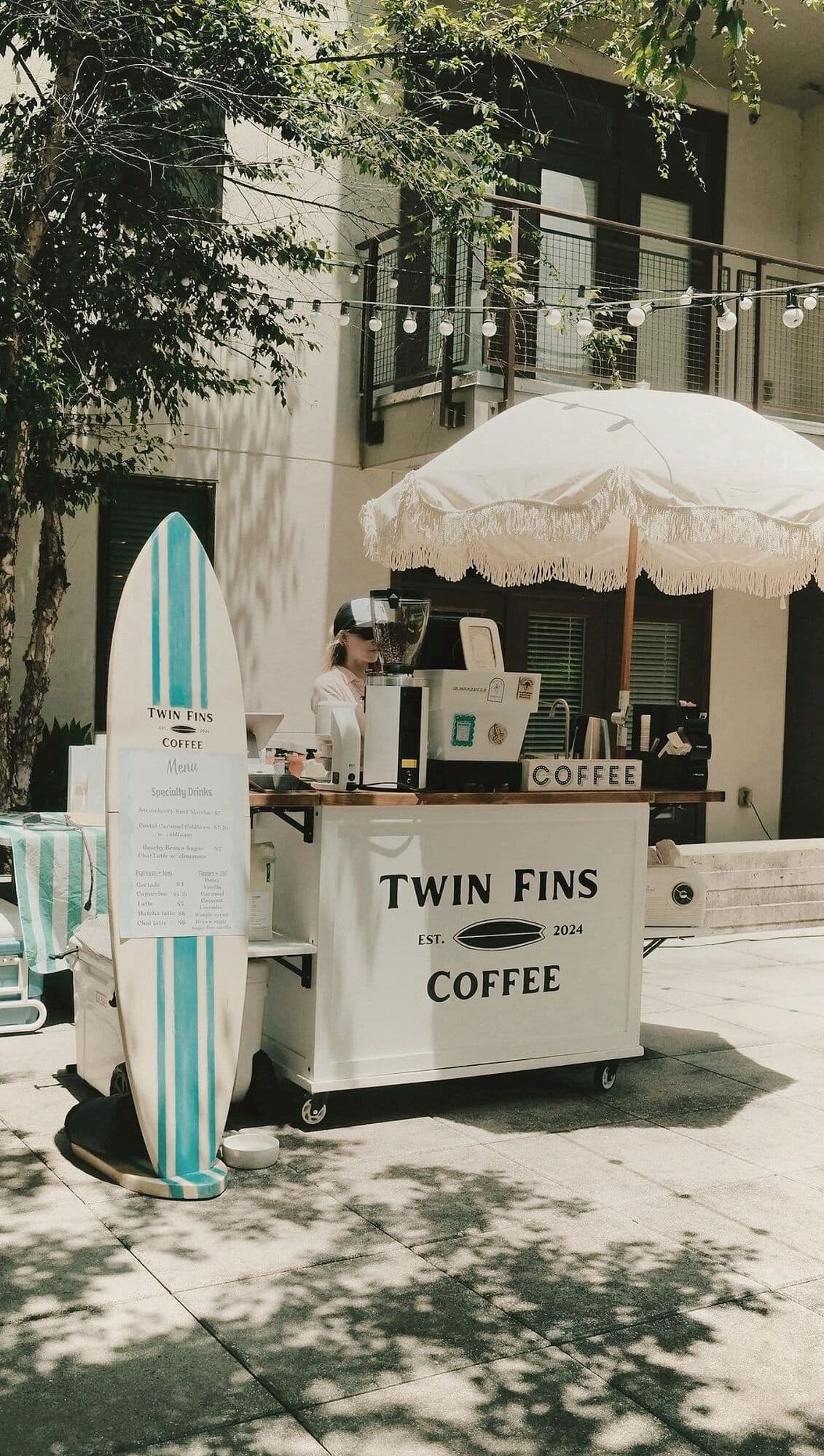 The Twin Fins cart on a shaded street with a longboard and fringed umbrella