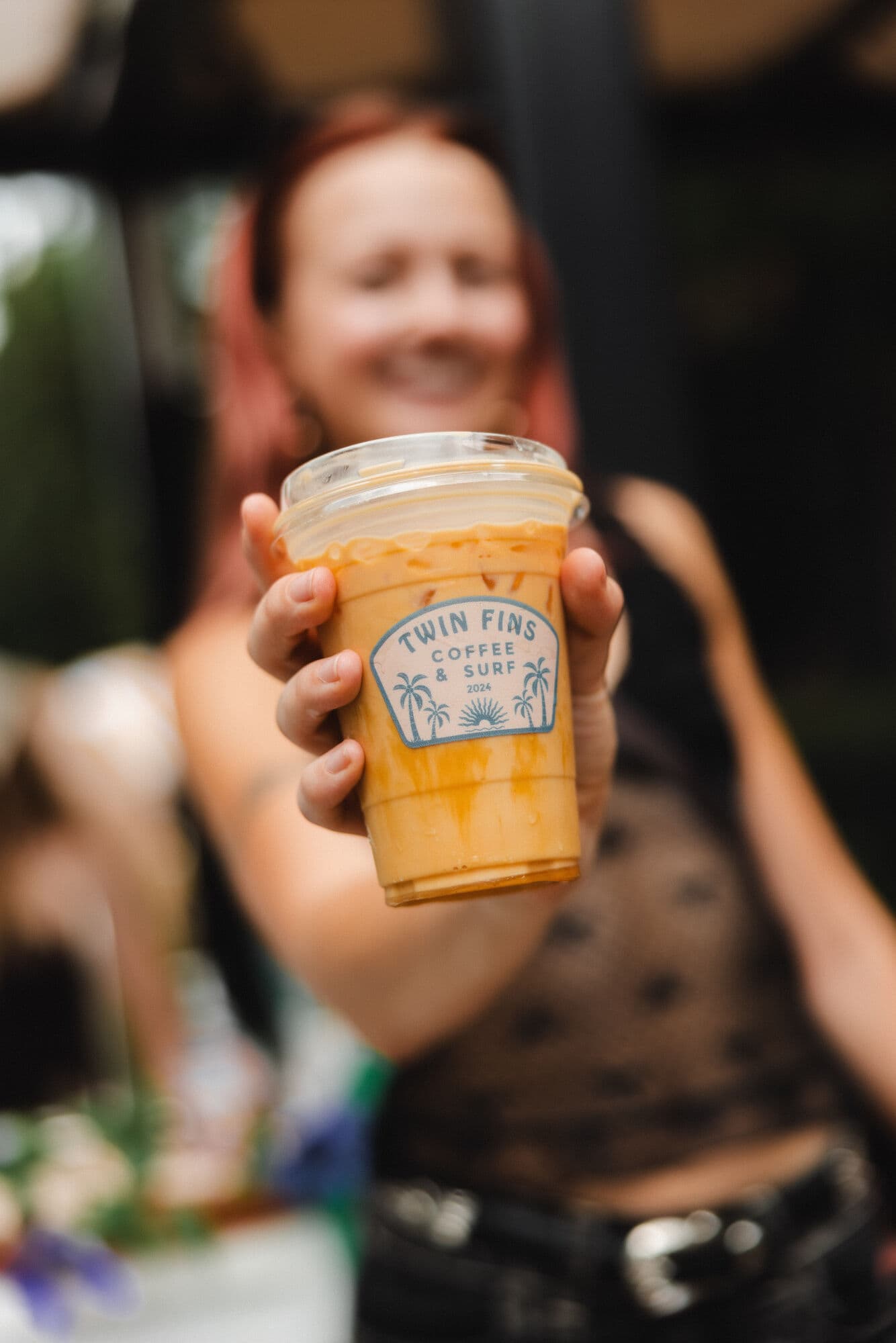 A guest holding up an iced latte in a branded Twin Fins cup