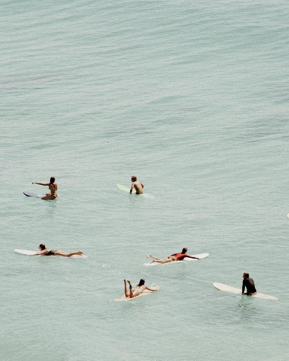 Surfers waiting in the lineup, seen from above on glassy green water