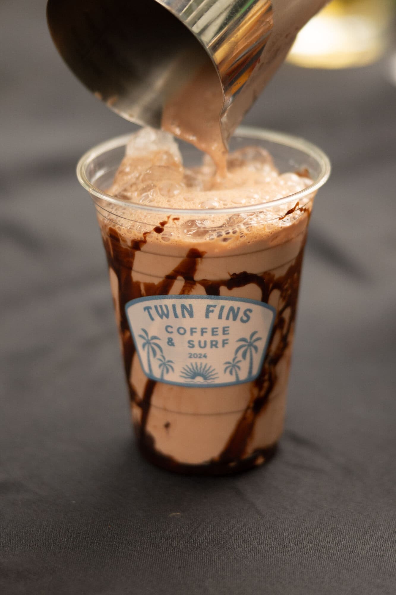 An iced mocha mid-pour, chocolate laced down the cup
