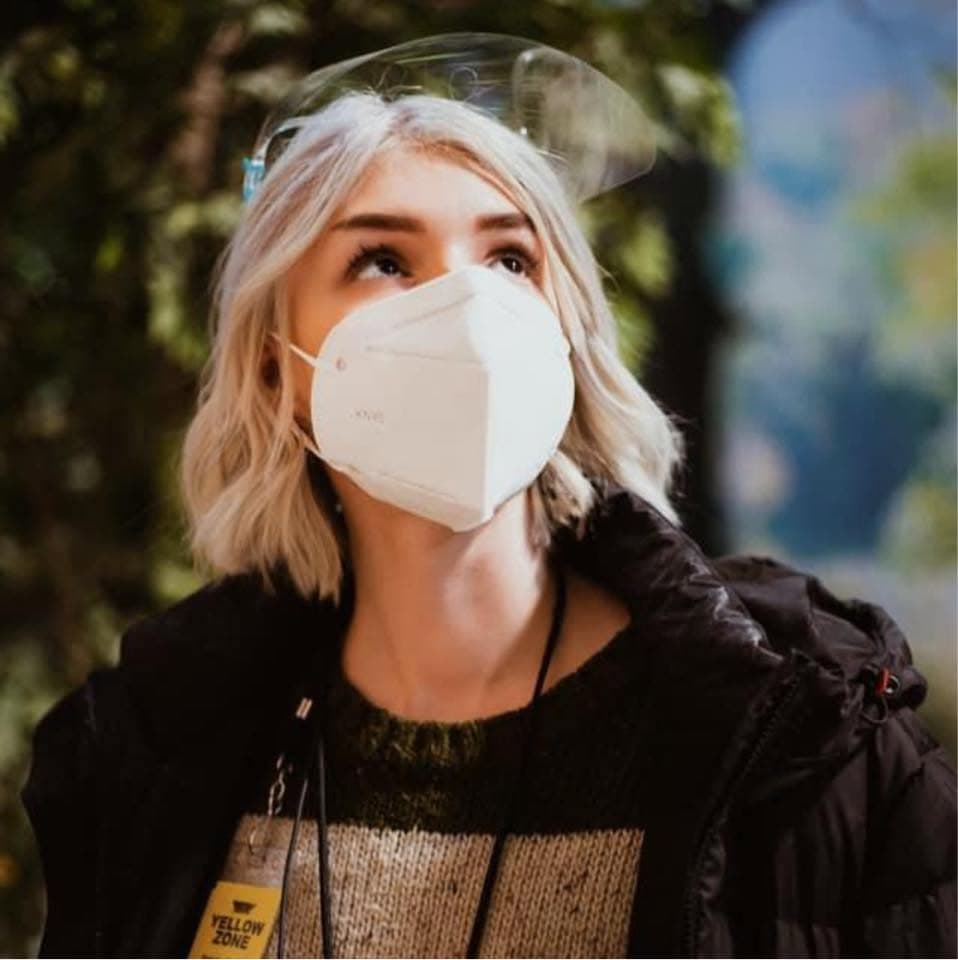 Natalia on a film set in a face shield and a Yellow Zone crew badge