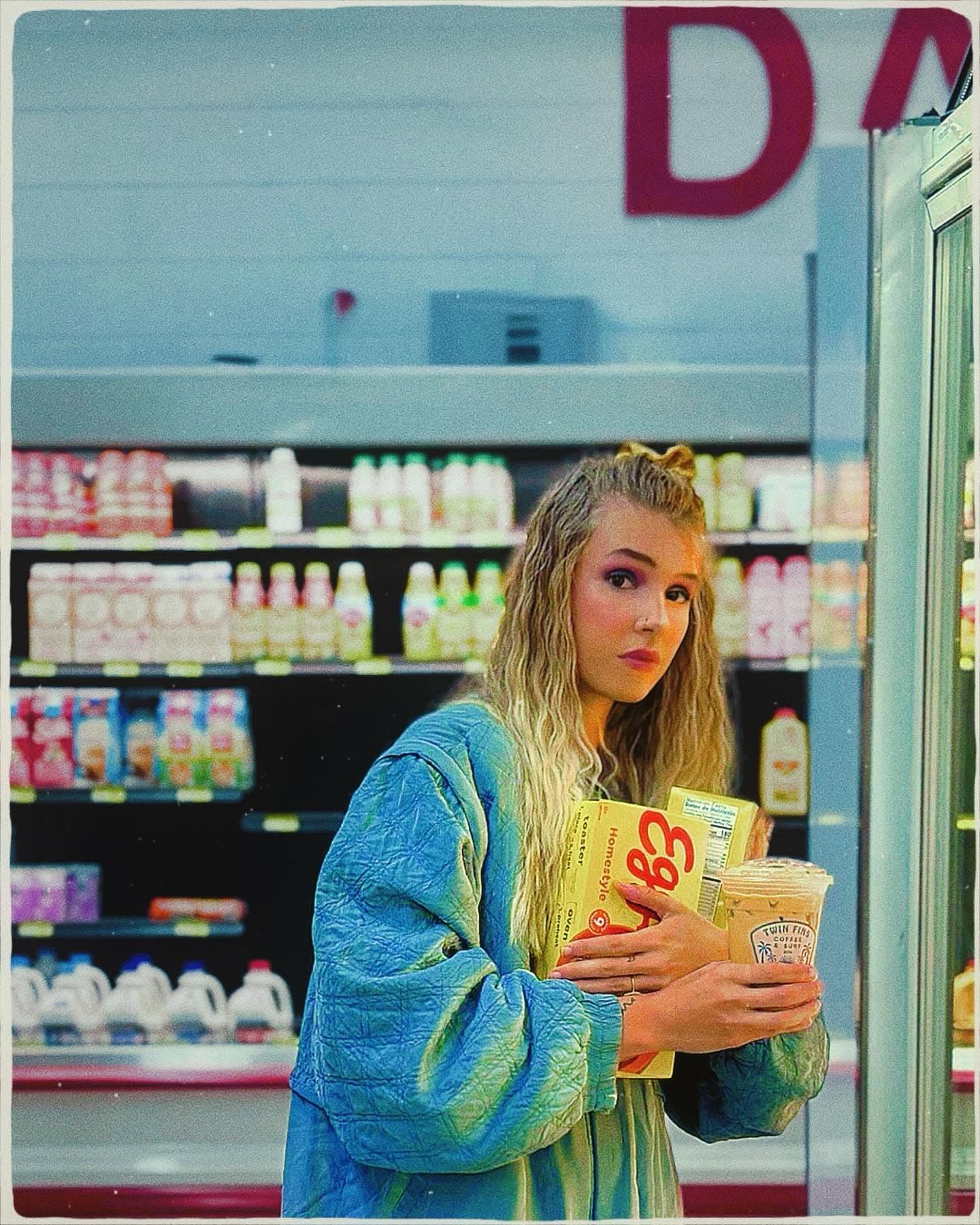 Natalia in an 80s jacket holding Eggo boxes and a Twin Fins cup in the dairy aisle