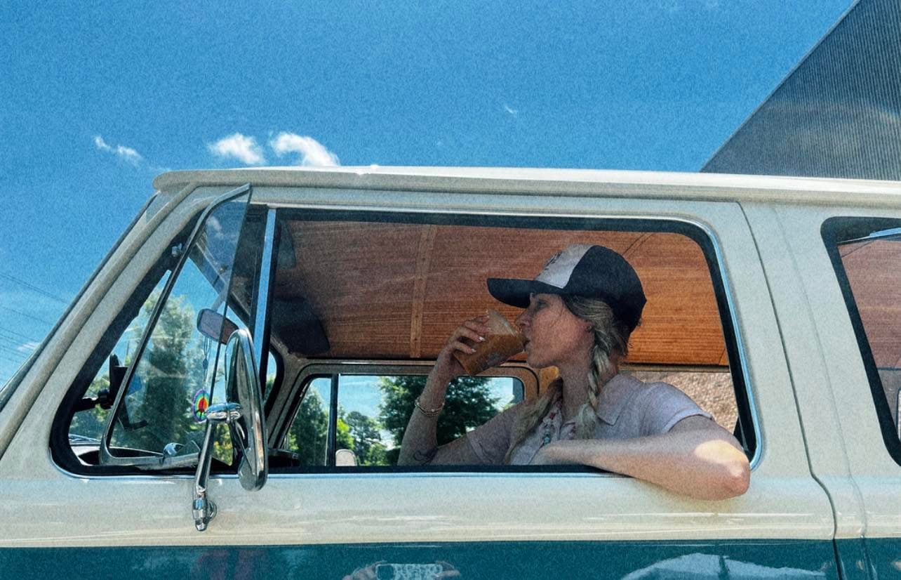 Natalia drinking an iced Twin Fins coffee from the window of a vintage van